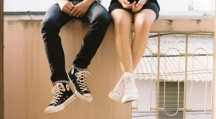 Two people sitting side by side on a ledge, legs dangling, representing a casual would you rather poll scenario.