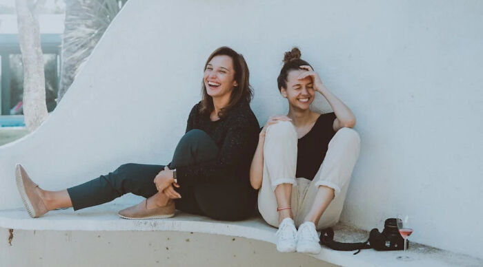 Two women sitting and laughing outdoors, enjoying a casual moment for a would you rather poll conversation.