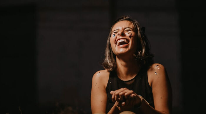 Young woman with confetti on her face smiling and laughing in a dark setting, capturing a fun would you rather poll moment