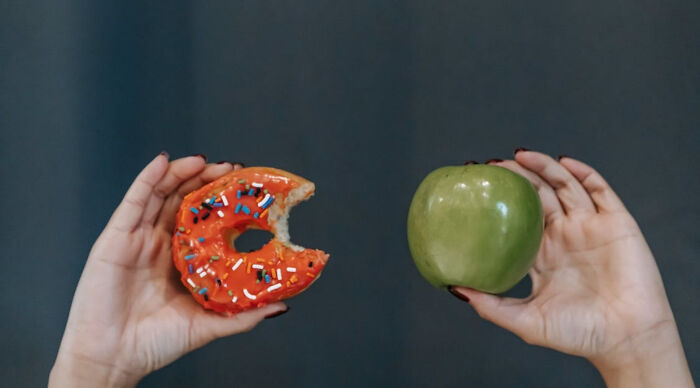 Hands holding a bitten sprinkled donut and a green apple representing a would you rather poll choice.