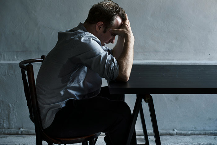 Man sitting at dark table with head in hands, symbolizing man wrongfully jailed and refusing to take down website.