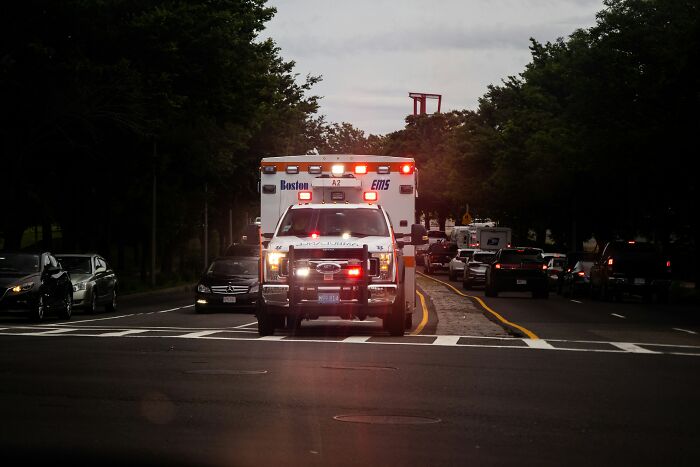 Ambulance with flashing lights driving through traffic at dusk, illustrating disturbing facts people shared.