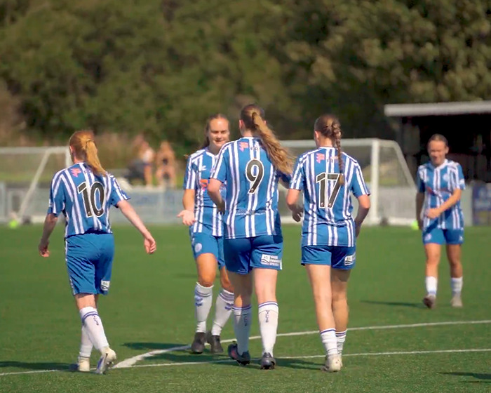16YO footballer celebrating on the field with teammates in blue and white striped kits during a daytime match. 16YO footballer celebrating on the field with teammates in blue and white striped kits during a daytime match.