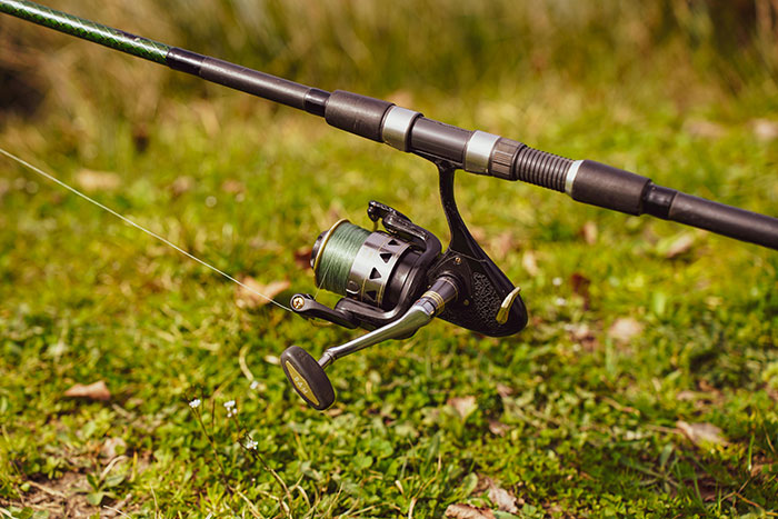 Fishing pole resting on green grass with reel and line extended, ideal for outdoor fishing activities.