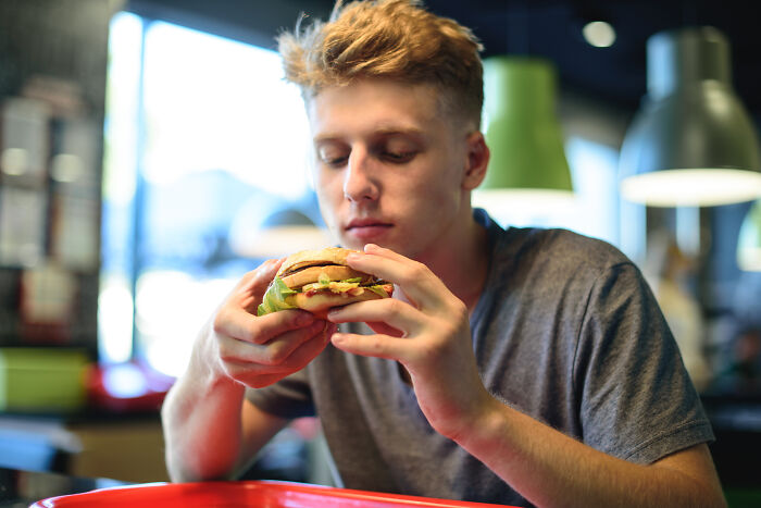 Young man in a casual setting examining a burger, illustrating 66 profession secrets that many people don't know about food industry.