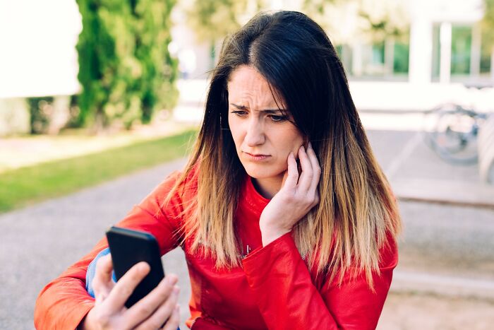Young woman in a red jacket looking at her phone with a worried expression, illustrating stories of savage rejection.