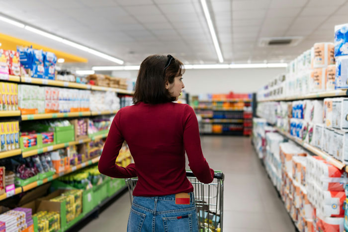 Woman pushing a shopping cart through supermarket aisles picking items for an American family grocery haul.