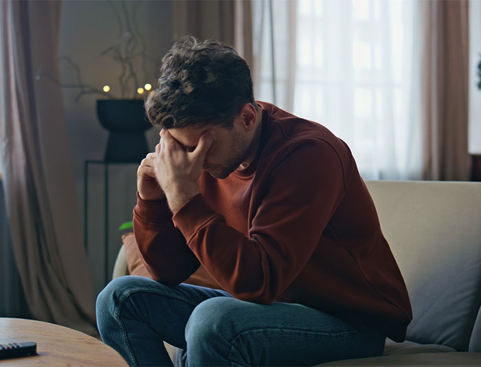 Man sitting on couch with head in hands, stressed and overwhelmed by a heavy secret before the wedding.
