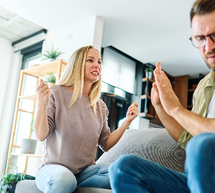 Couple arguing on couch, frustrated woman calling out lazy guy who refuses to listen in modern living room.