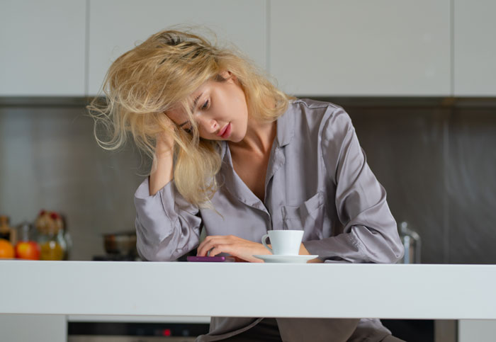 Woman in pajamas looking stressed and tired at kitchen table, reflecting on fears about motherhood challenges. Woman in pajamas looking stressed and tired at kitchen table, reflecting on fears about motherhood challenges.