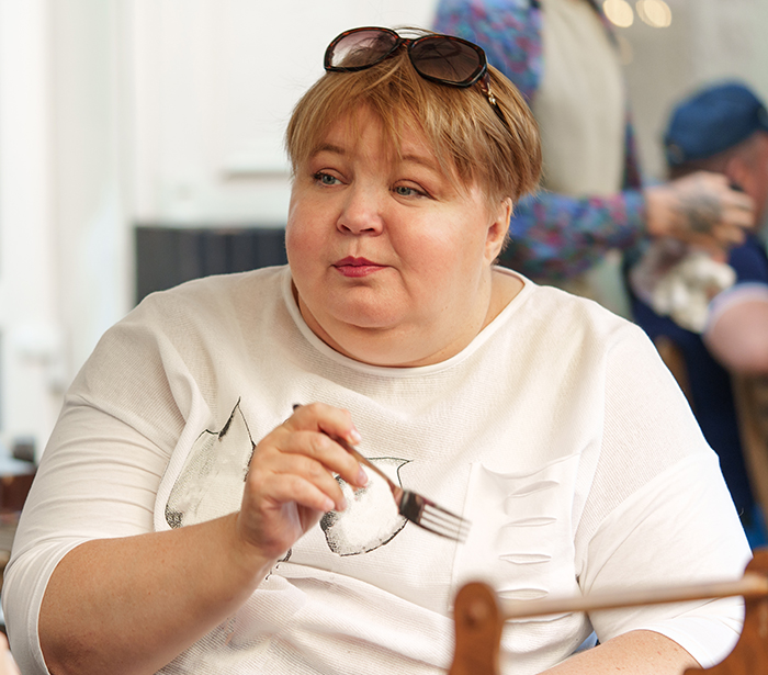 Woman in white shirt holding a fork at a table, reflecting on a man breaking up after an argument about cheese.