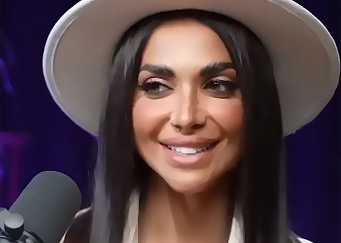 Influencer smiling and speaking into a microphone while wearing a white hat during a live recording session.