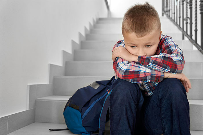 Sad young boy sitting on school stairs with backpack, capturing a moment related to mom furious over school call and CPS concern. Sad young boy sitting on school stairs with backpack, capturing a moment related to mom furious over school call and CPS concern.