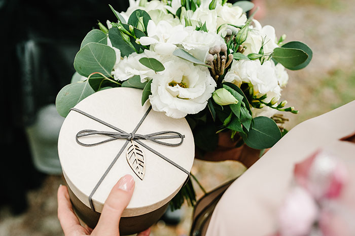 Bride holding bouquet of white flowers and round gift box tied with string, related to wedding shower gifts controversy.