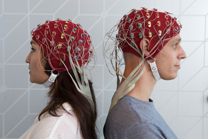 Two people wearing red EEG caps with wires, illustrating scientific study on gut feeling and precognition research.
