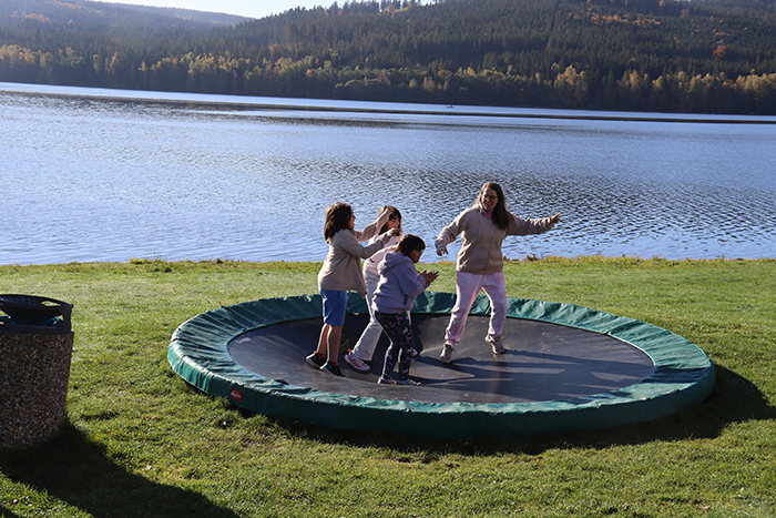 Four children playing together on a trampoline by a lake, illustrating family dynamics with sister accuse favoring nephew niece theme.