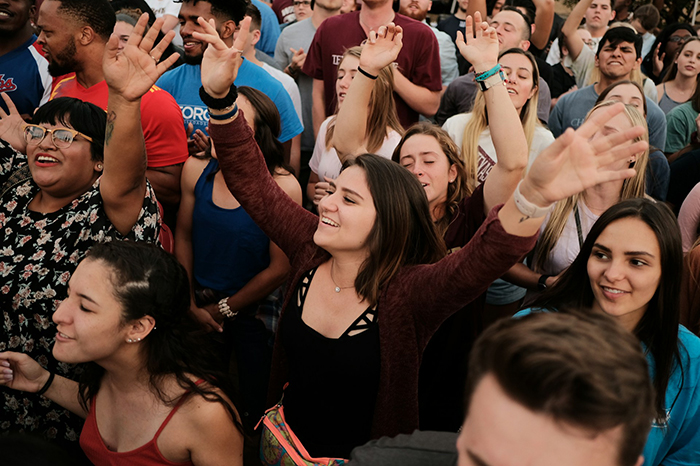 A diverse group of young people at a lively outdoor event, woman raising hands with joyful expression. A diverse group of young people at a lively outdoor event, woman raising hands with joyful expression.
