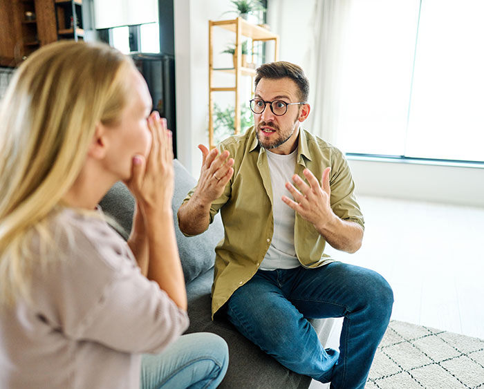 Man giving wife an ultimatum about plastic surgery, couple arguing intensely in a bright living room setting.
