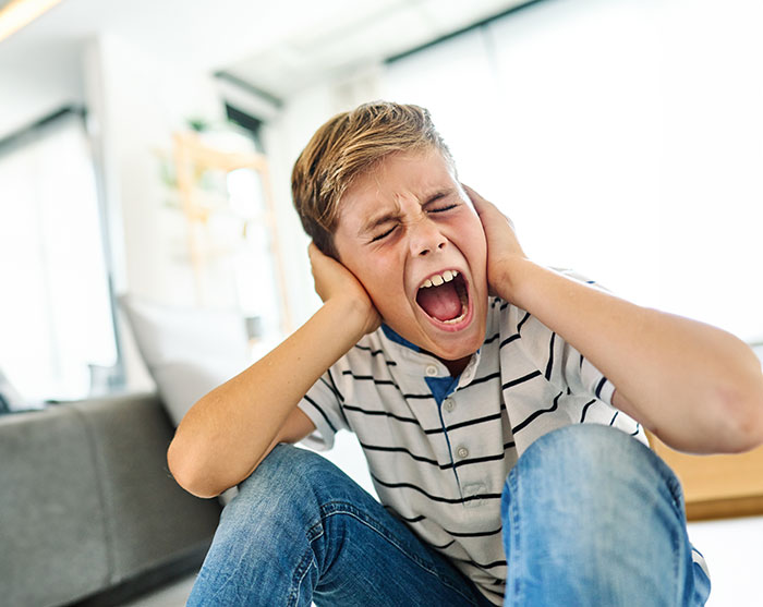 Young boy having a meltdown indoors covering ears upset about mountain biking early in the morning.