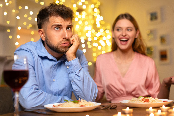 Man looking frustrated on a date with a woman at a candlelit dinner, hiding a horrible reason for cutting it short.