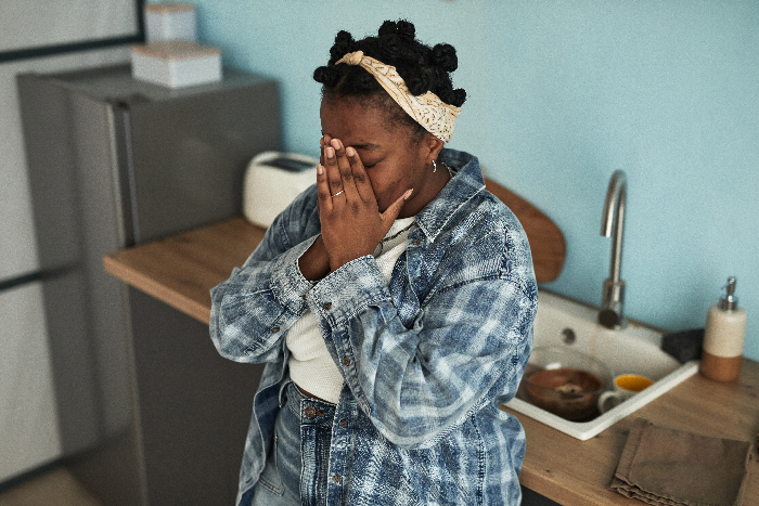 Stressed single mom in kitchen covering face, reflecting emotions related to abandoning toddler and parents to restart life.