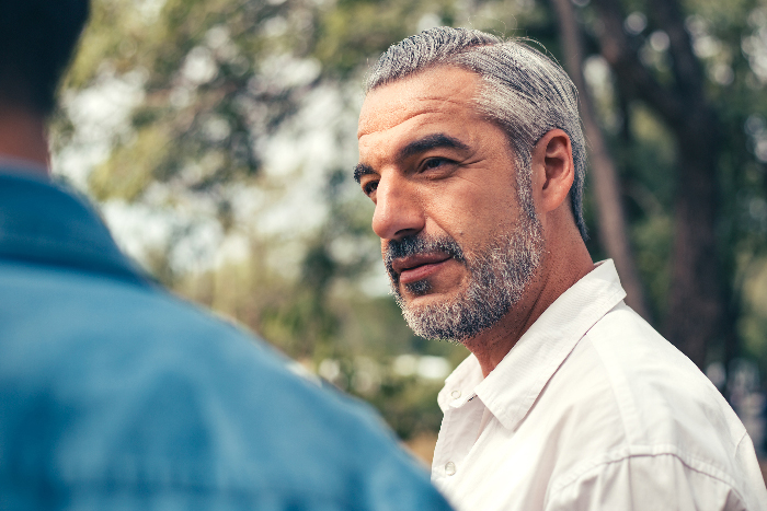 Man with gray hair and beard confidently confronting someone outdoors, symbolizing crushing former bully&rsquo;s ego at reunion.