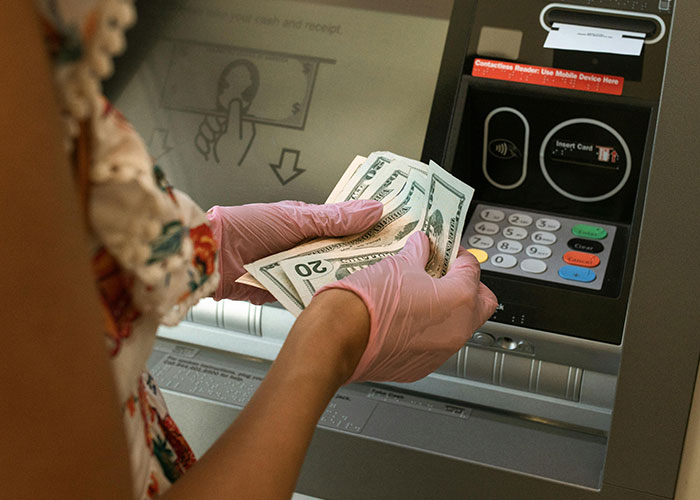 Person wearing pink gloves counting cash at an ATM machine in a scene related to criminal fails.