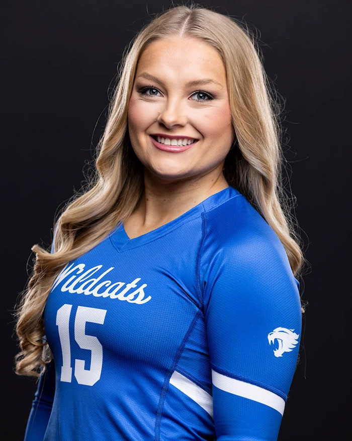 Cheerleader in blue Wildcats jersey smiling against a dark background, representing university athletics.