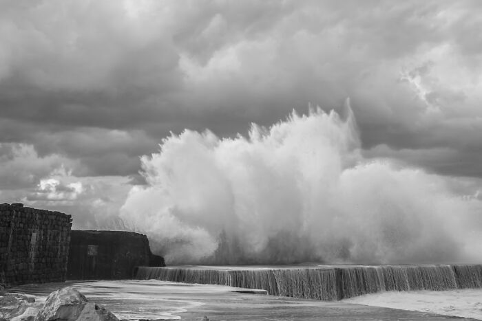 Stormy coastal scene with large waves crashing near a stone pier, symbolizing chaotic experiences of food delivery drivers.