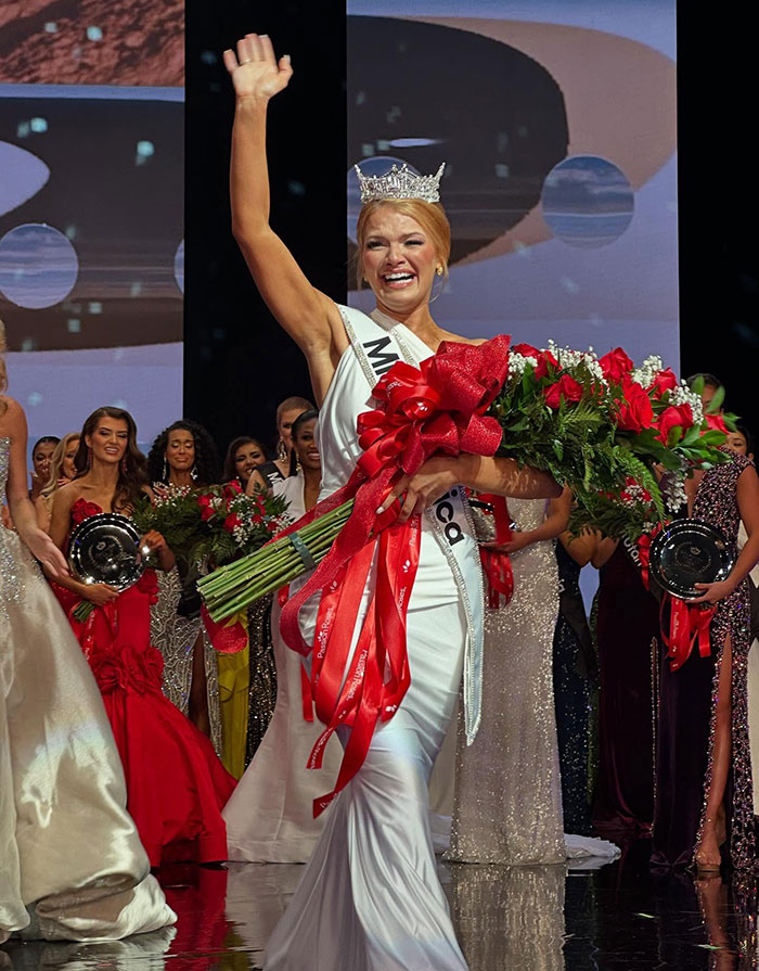 Newly crowned Miss America waving with bouquet of roses on stage at beauty pageant event. Newly crowned Miss America waving with bouquet of roses on stage at beauty pageant event.