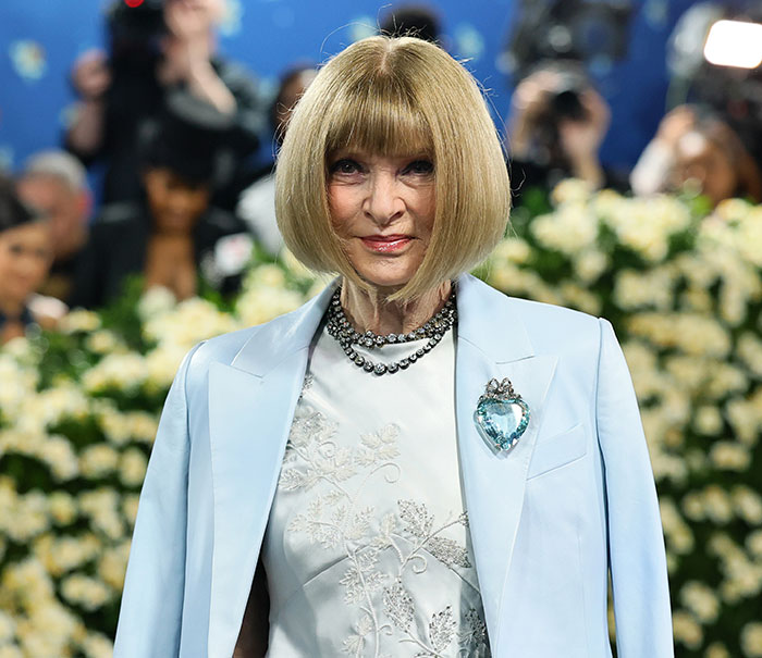 Anna Wintour at a fashion event, wearing a light blue blazer and statement necklace, embodying iconic style.