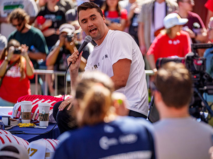 Man speaking into microphone at outdoor event with crowd, related to FBI update on Charlie Kirk assassination sniper evidence.