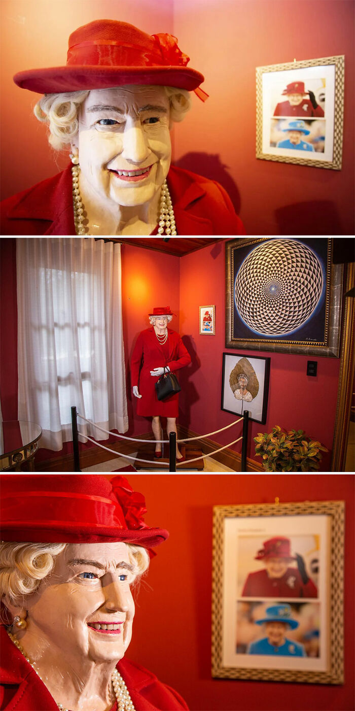 Wax sculpture of a famous figure wearing a red hat and outfit, displayed in a room with framed pictures and art.
