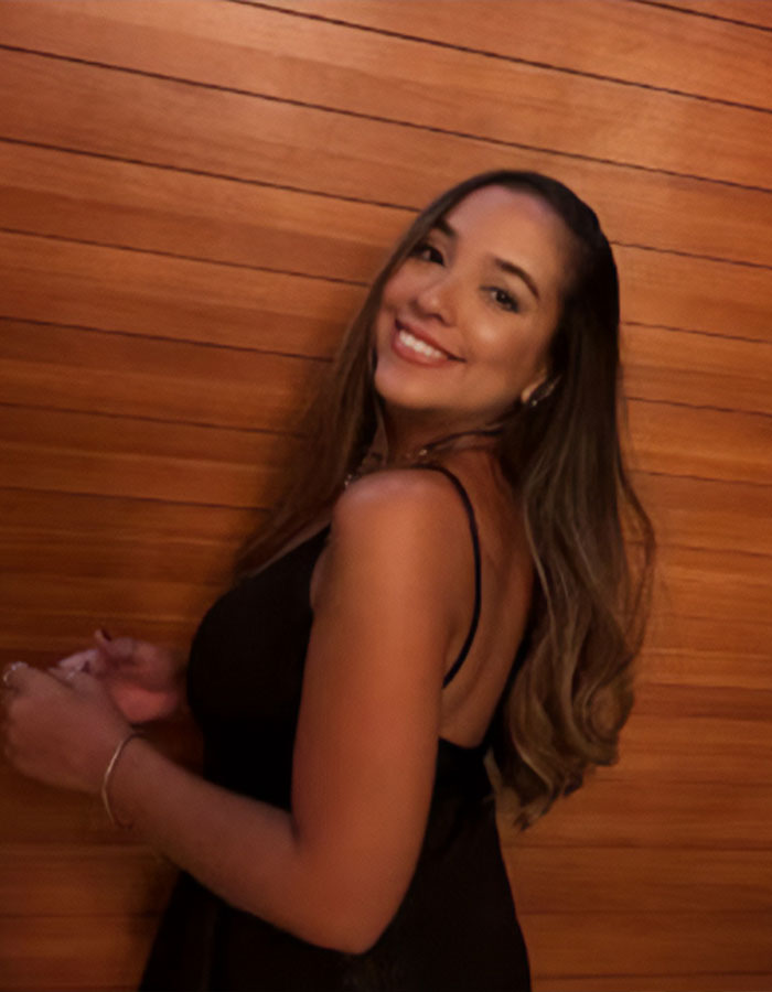 Smiling woman posing by wooden wall, highlighting plastic surgeon arrest after mom's butt lift procedure goes wrong.