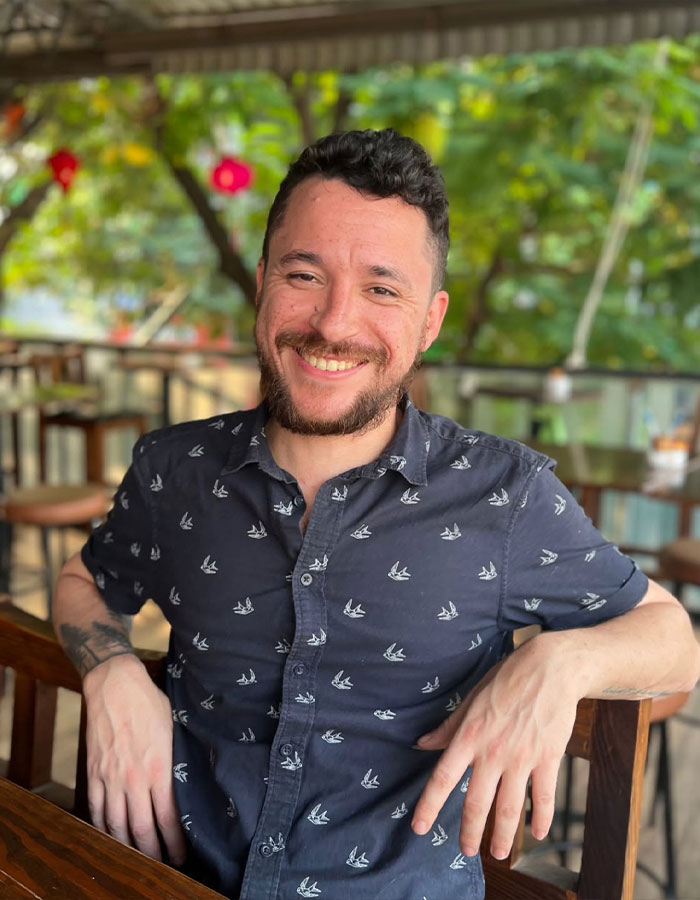 Smiling man in a patterned shirt sitting outdoors, representing a tragic twist in poisoned limoncello case seeking justice.