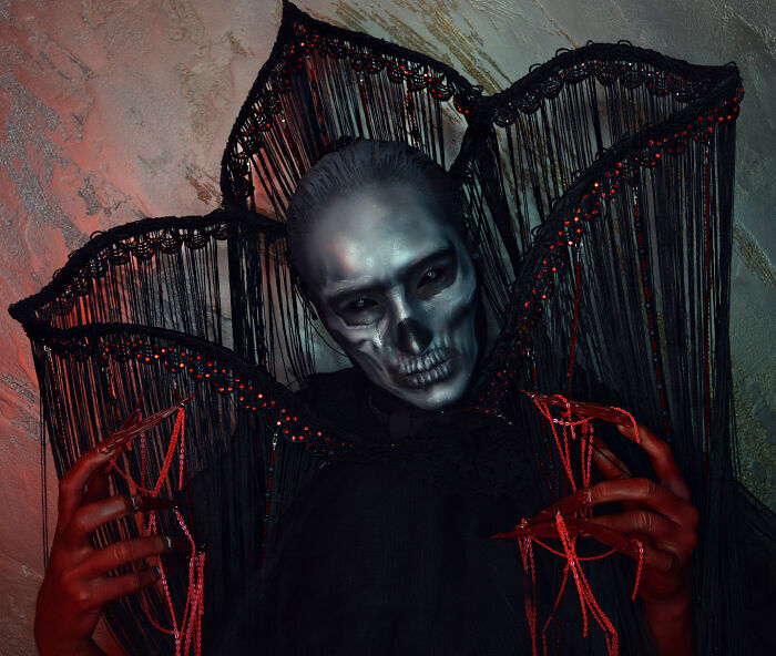 Person with haunting Halloween makeup and costume featuring skull face paint and elaborate black and red details.