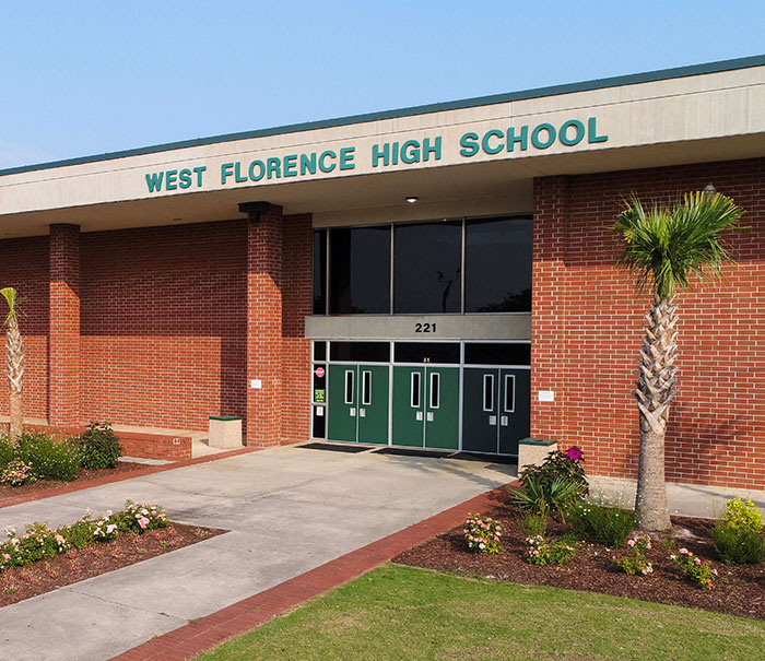 Entrance of West Florence High School with brick walls and green doors, related to teacher arrested for using poop spray incident.