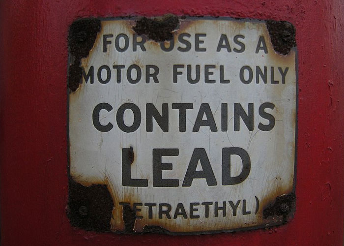 Rusty vintage sign on red background warning motor fuel contains lead, highlighting historical events with damage to society.