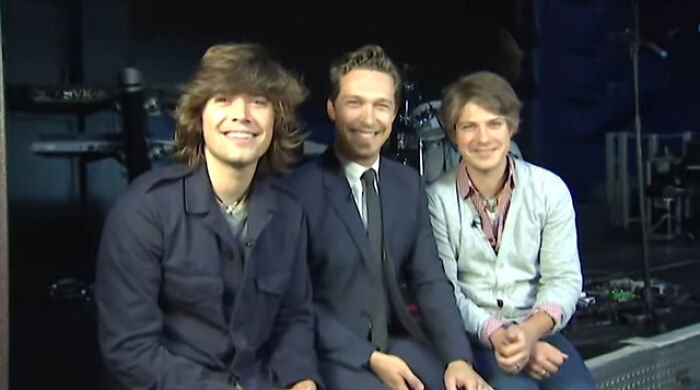 Three young men smiling together on stage, capturing a memorable moment meeting an idol experience.