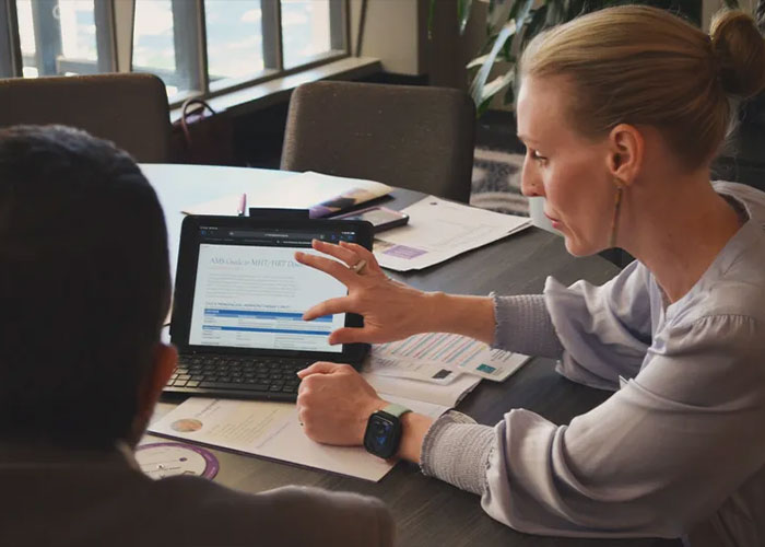 Two professionals discussing health risks of breastfeeding stigma while reviewing information on a tablet at a workspace.