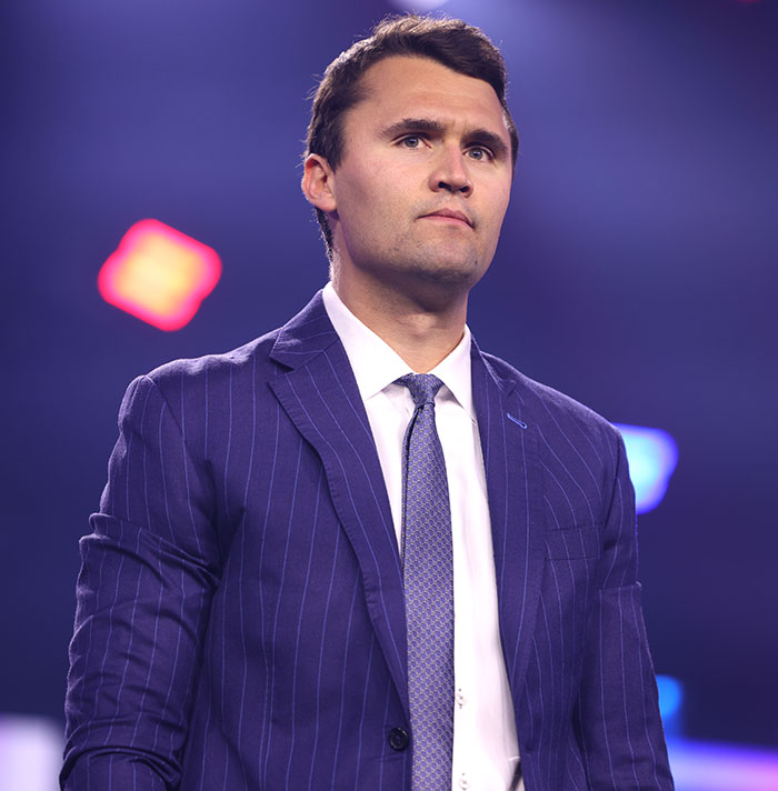 Man in a pinstripe suit and tie standing on stage, related to sisters who destroyed Charlie Kirk memorial story.