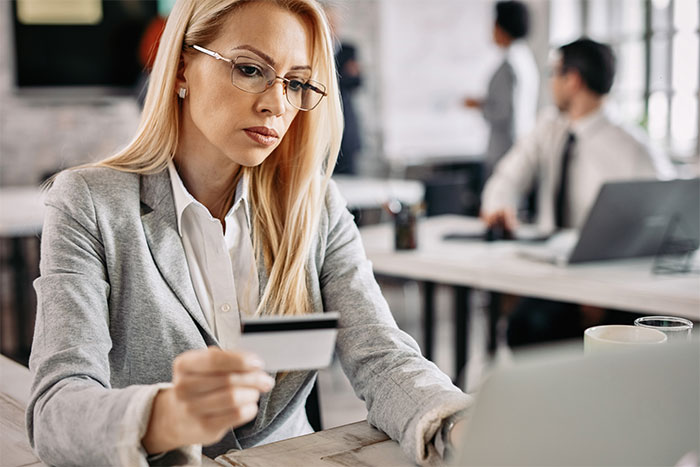Businesswoman with glasses using credit card online, illustrating advanced stupid out-of-touch moments in modern work settings.