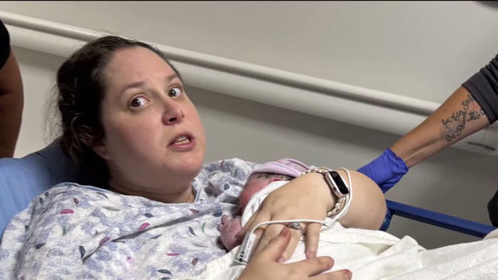 Woman holding newborn in hospital bed, surprised after unexpectedly delivering her third child without knowing she was pregnant.