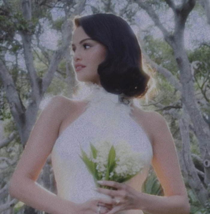 Selena Gomez in a white halter wedding dress holding flowers at Billy Blanco's star-studded wedding outdoors.