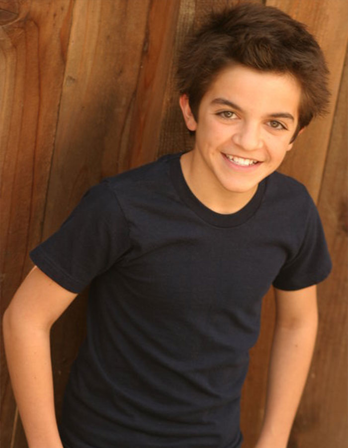 Young Nickelodeon actor smiling outdoors wearing a dark shirt with a wooden fence background for homeless fundraiser.