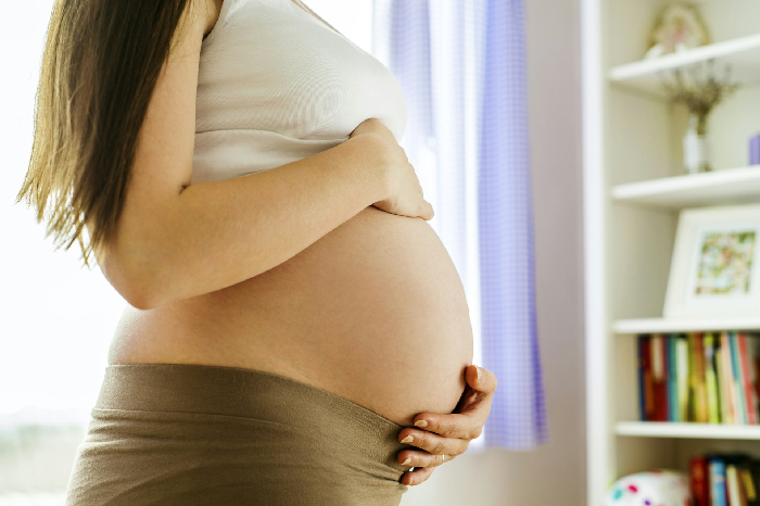 Pregnant woman gently holding belly in softly lit room, highlighting challenges faced by husband and baby in family dynamics.
