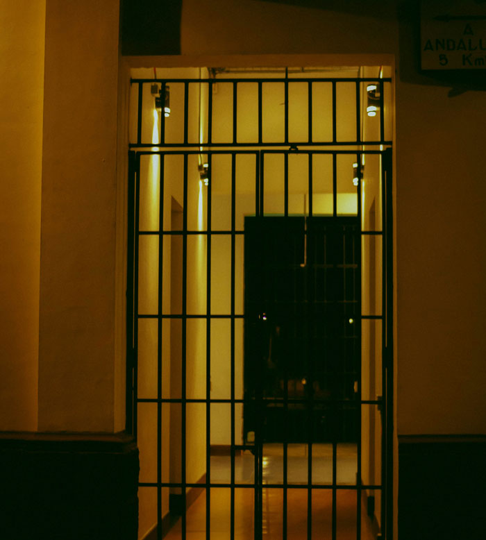 Dimly lit jail cell behind black iron bars, representing police and cops witnessing horrible events.