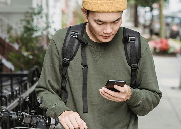 Young man wearing a beanie and backpack looking at phone on city street, illustrating incredible coincidences concept