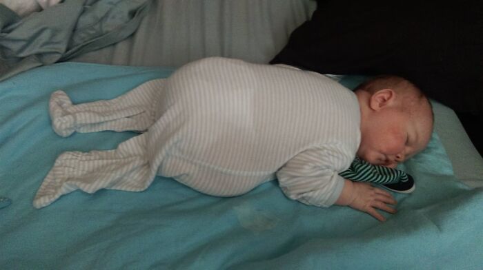 Sleeping baby in cozy striped pajamas resting on blue bedding, a wholesome moment to brighten your day.