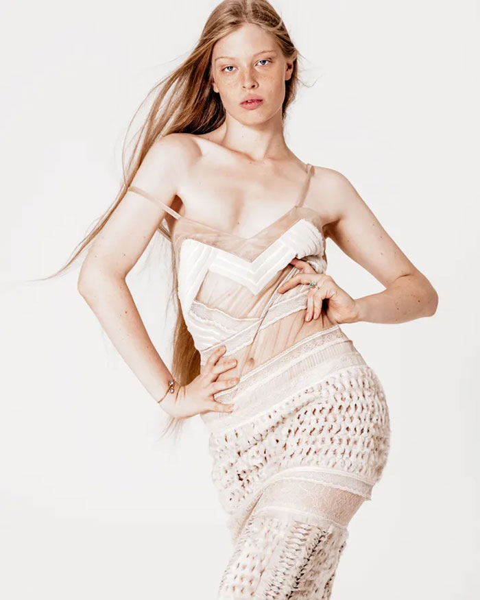 Elon Musk’s transgender daughter posing confidently in a sheer, textured white outfit against a plain background. Elon Musk’s transgender daughter posing confidently in a sheer, textured white outfit against a plain background.